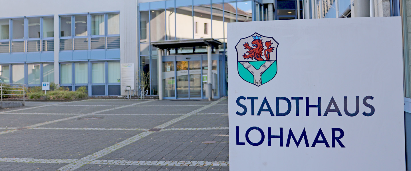 Ein Foto vom Eingang des Rathaus von Lohmar mit dem Schild des Rathauses davor.